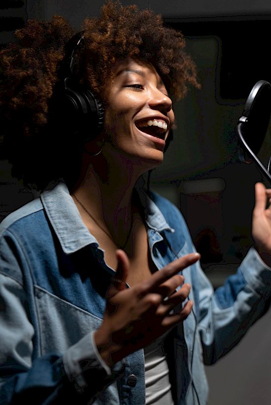 A person wearing headphones is singing into a microphone in a recording studio, looking expressive and engaged.