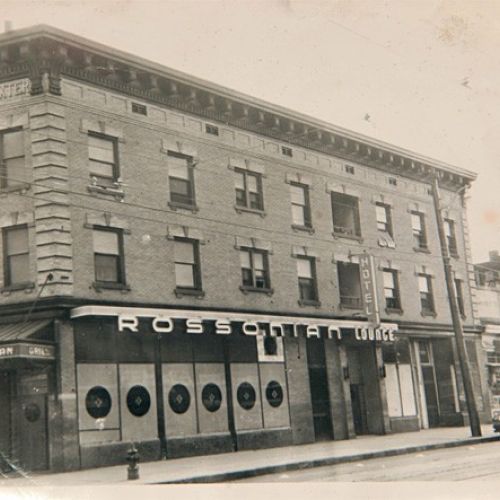 A vintage black-and-white image of the Rossonian Hotel on a street corner, featuring signage and classic architectural details.