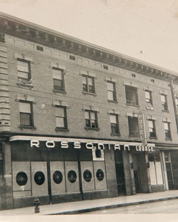 A vintage black-and-white image of the Rossonian Hotel on a street corner, featuring signage and classic architectural details.